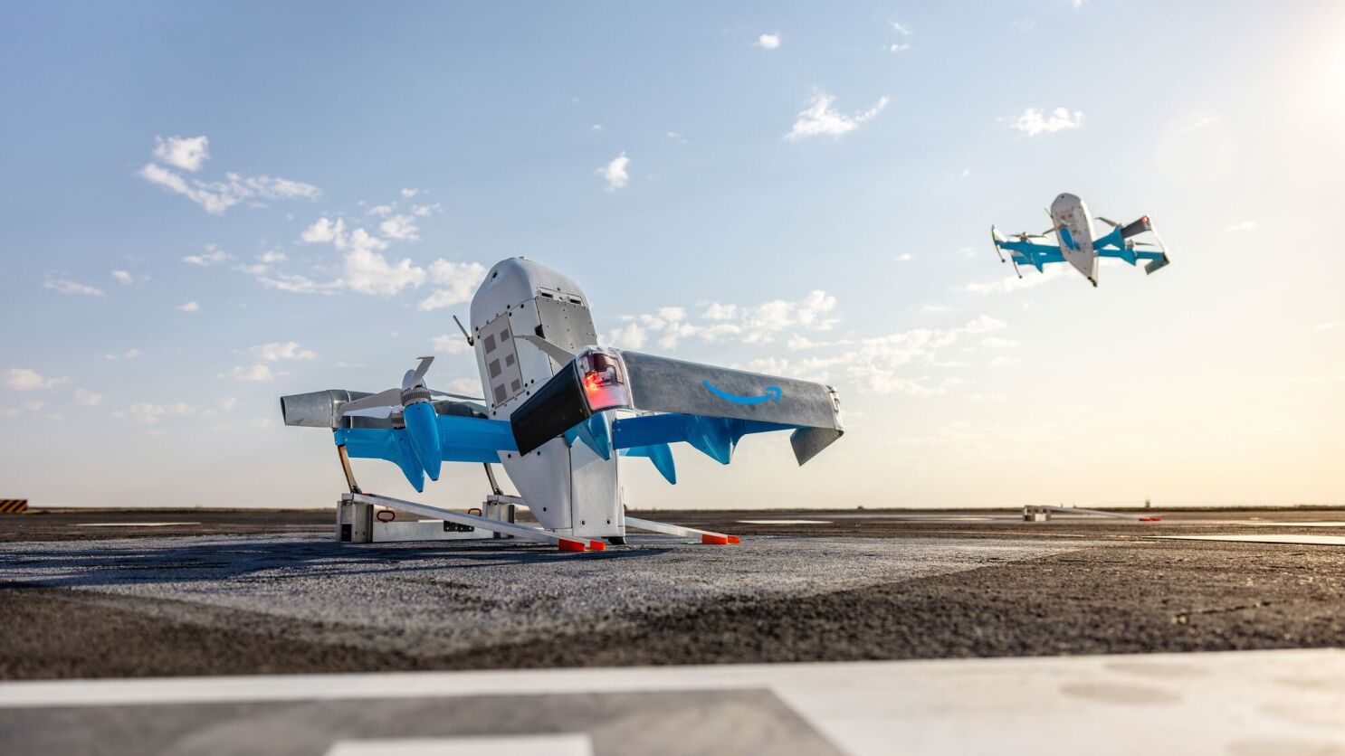 Un dron Amazon Prime Air MK30 en su riel de lanzamiento con otro en vuelo.