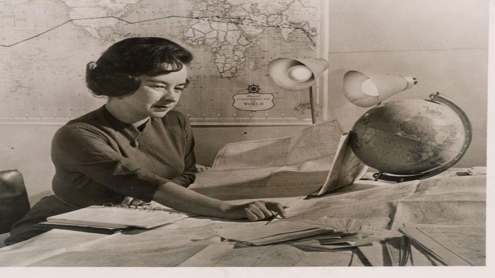 Jerrie Mock planeando su vuelo alrededor del mundo, enero de 1964. Jerrie Mock estudia cartas náuticas junto a un globo terráqueo y un mapamundi mientras planea su vuelo en solitario alrededor del mundo, enero de 1964.