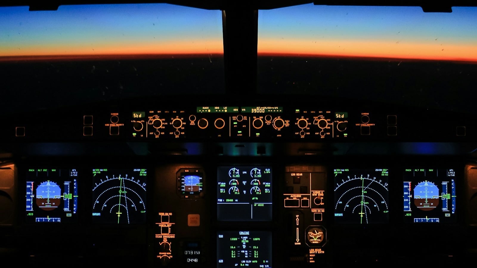 An airliner flight deck at cruise altitude at night, the altitude window showing 39,000 feet and the horizon lit by sunrise