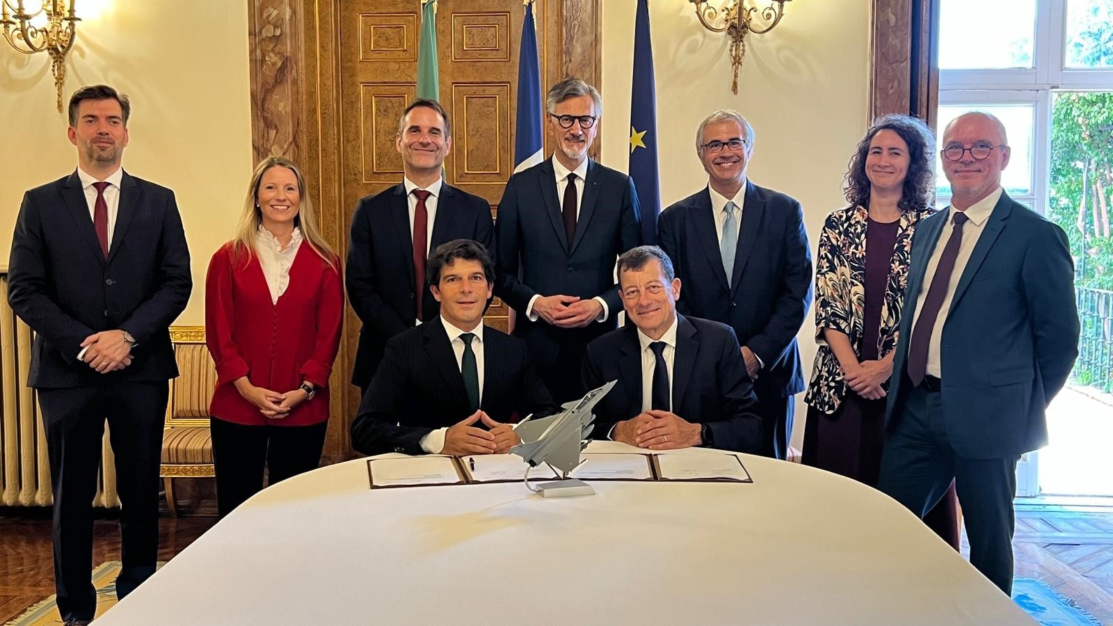 Signatories seated with a Rafale model between them at the French Embassy in Lisbon, delegation standing behind