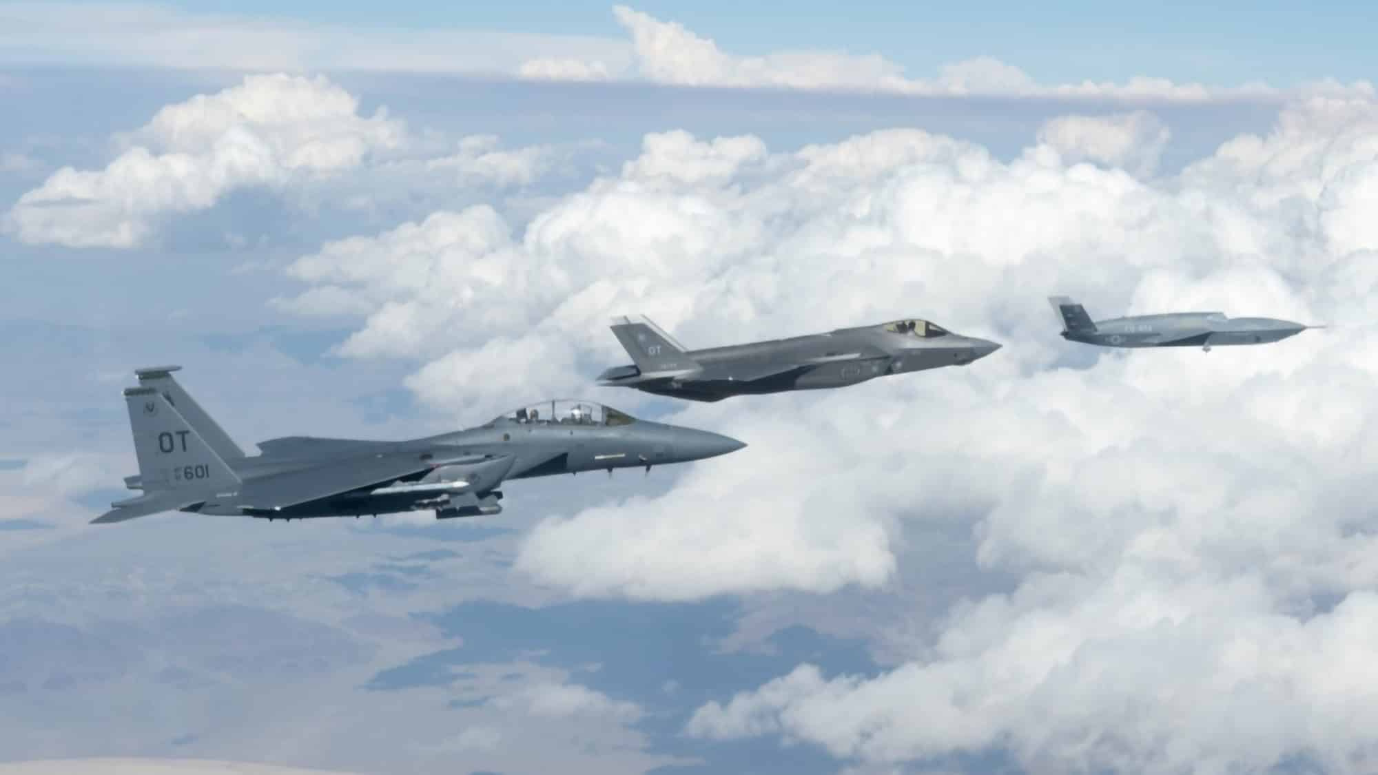 A General Atomics FQ-42 Vengeance collaborative combat aircraft flying in formation with a US Air Force F-35A Lightning II and an F-15E Strike Eagle above cloud