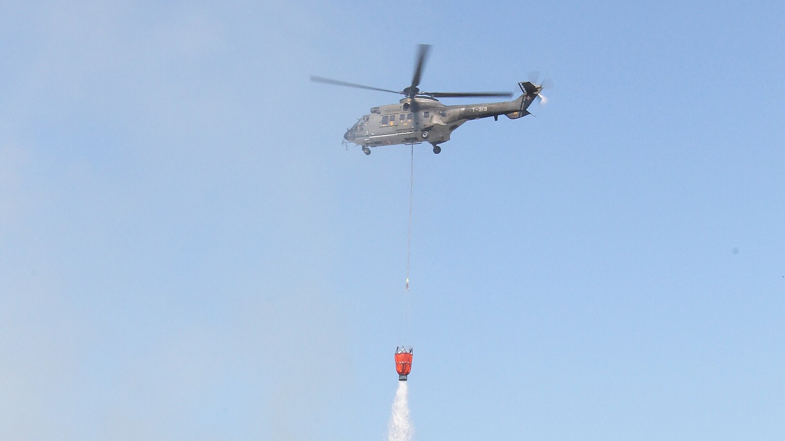 An AS332 Super Puma helicopter releasing water from an underslung bucket