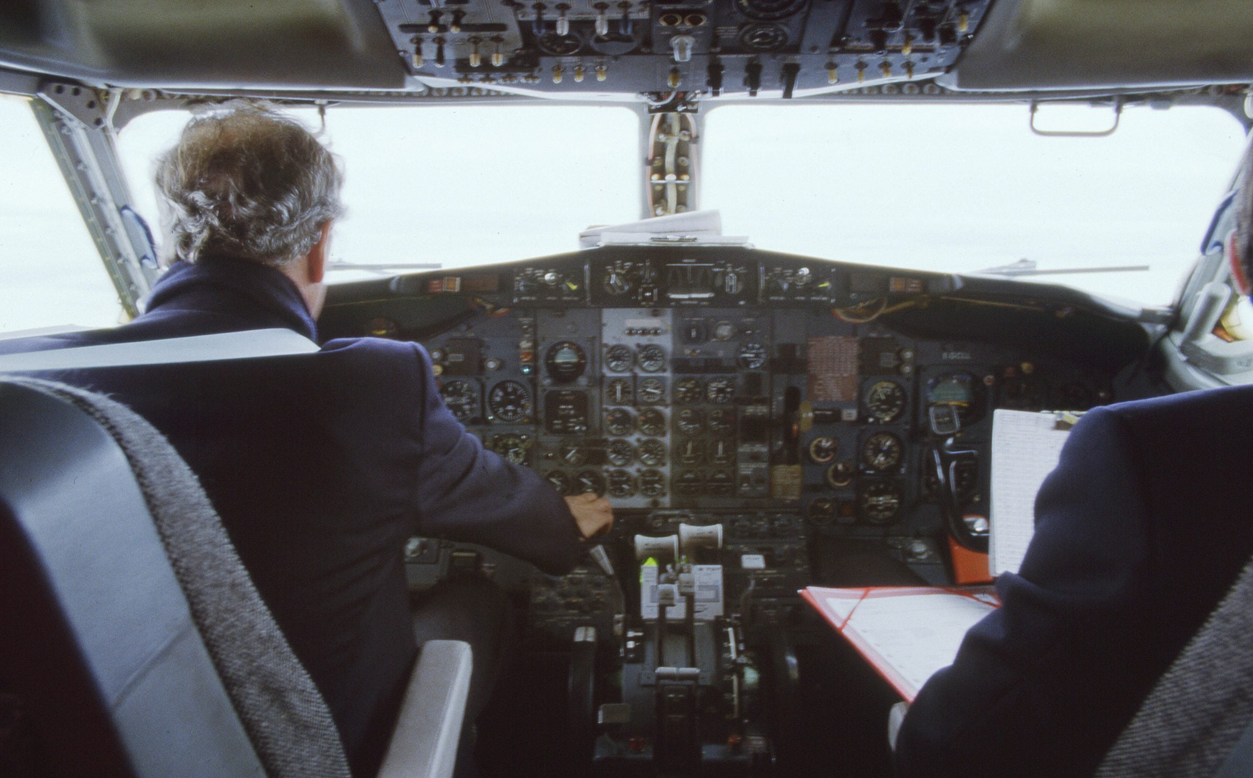 Airline captain at the controls A grey-haired airline captain flying a Boeing 737 from the left seat, seen from behind