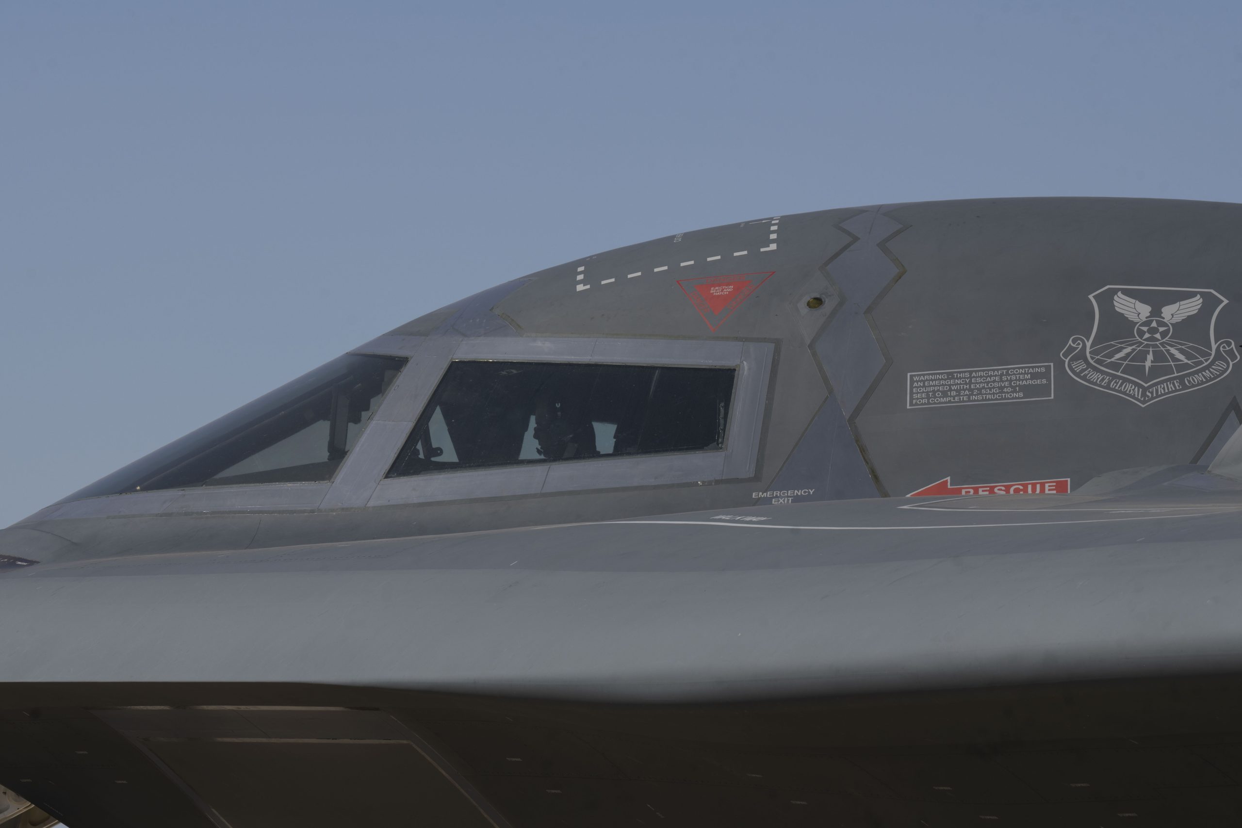 The nose and cockpit windows of a B-2 Spirit stealth bomber with a crew member visible inside