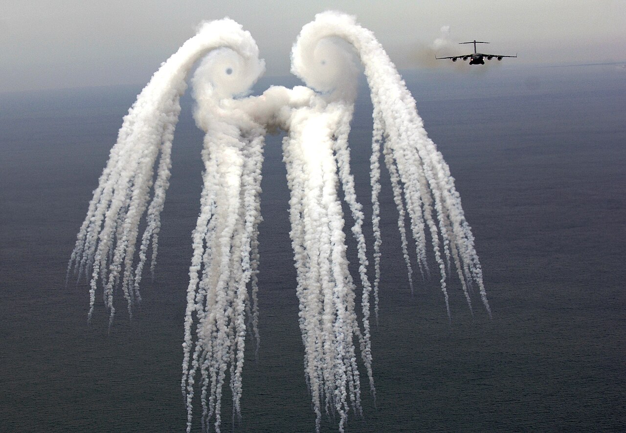 Un C-17 de la Fuerza Aérea de EE. UU. lanzando bengalas sobre el Atlántico; el humo revela los vórtices de las puntas de las alas.