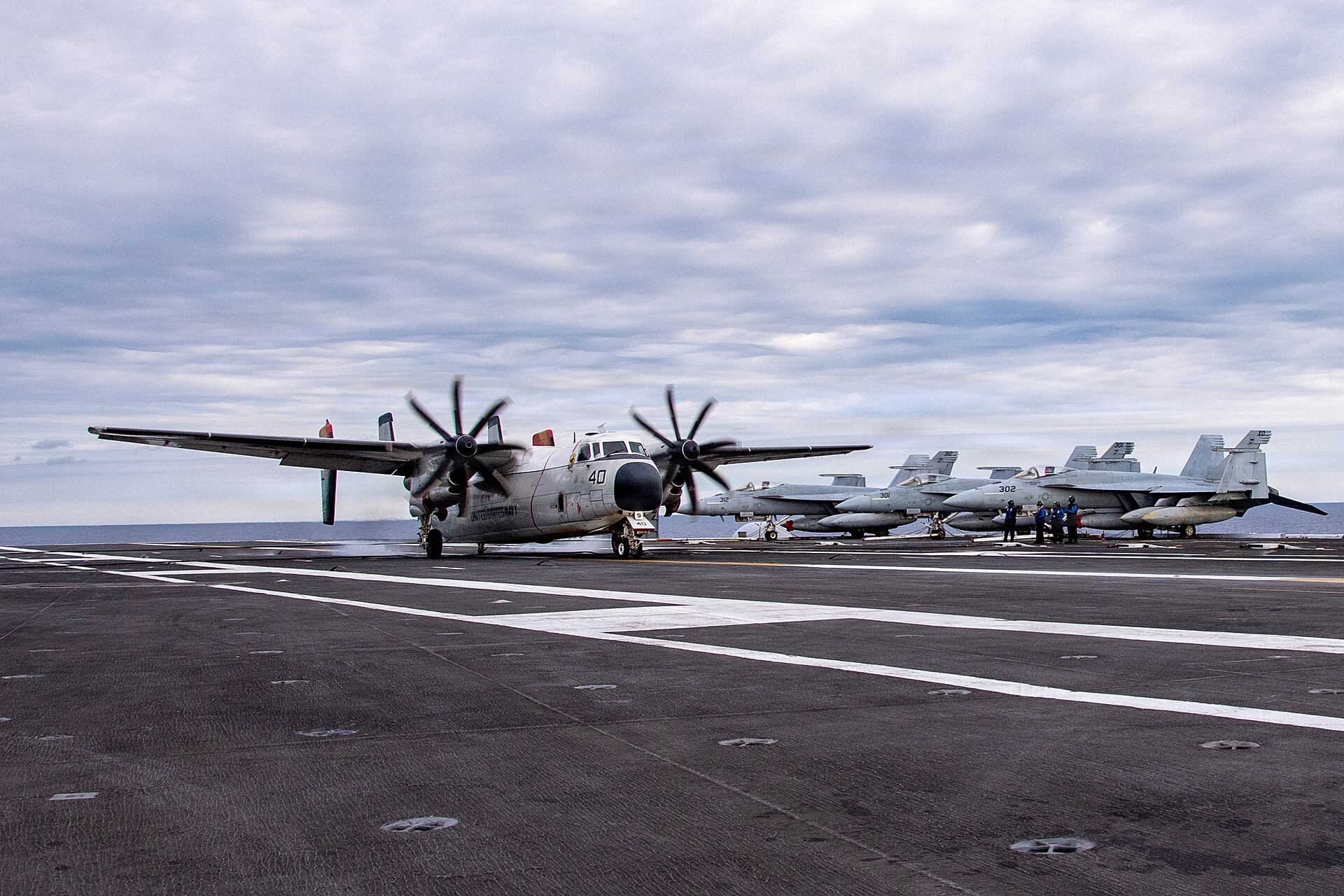 A US Navy C-2A Greyhound on a carrier flight deck with Super Hornets parked behind it