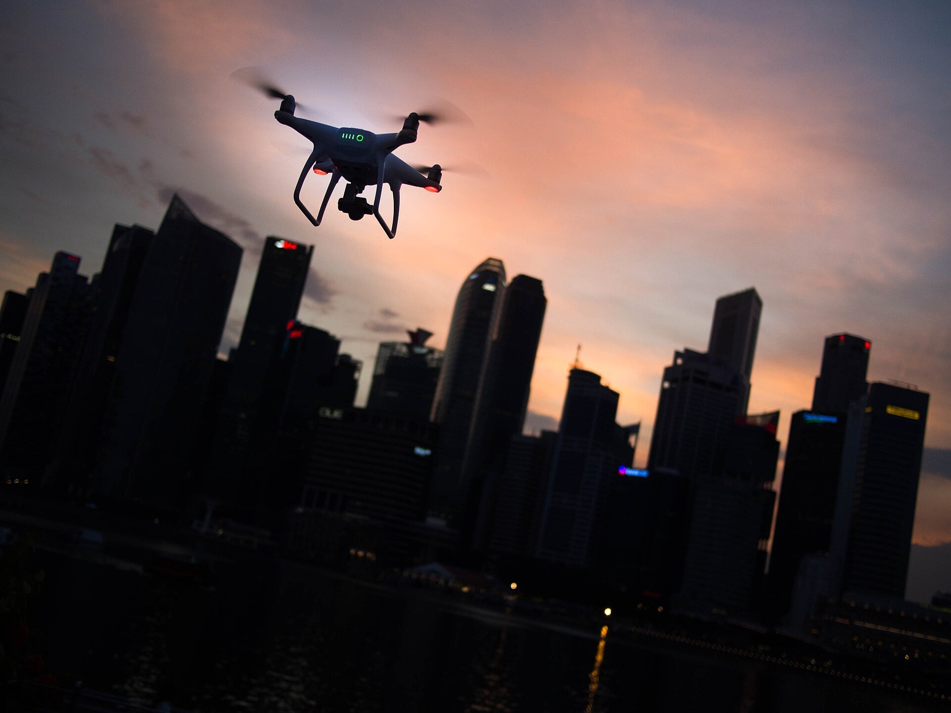 A small consumer drone silhouetted against the sky at dusk