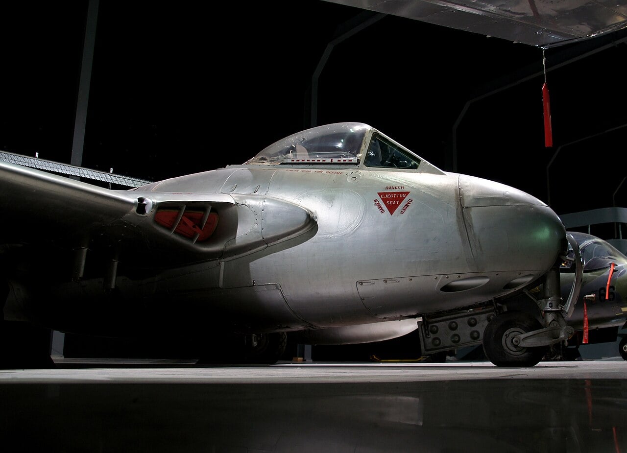 A bare-metal de Havilland Vampire jet fighter with its twin-boom tail, preserved indoors