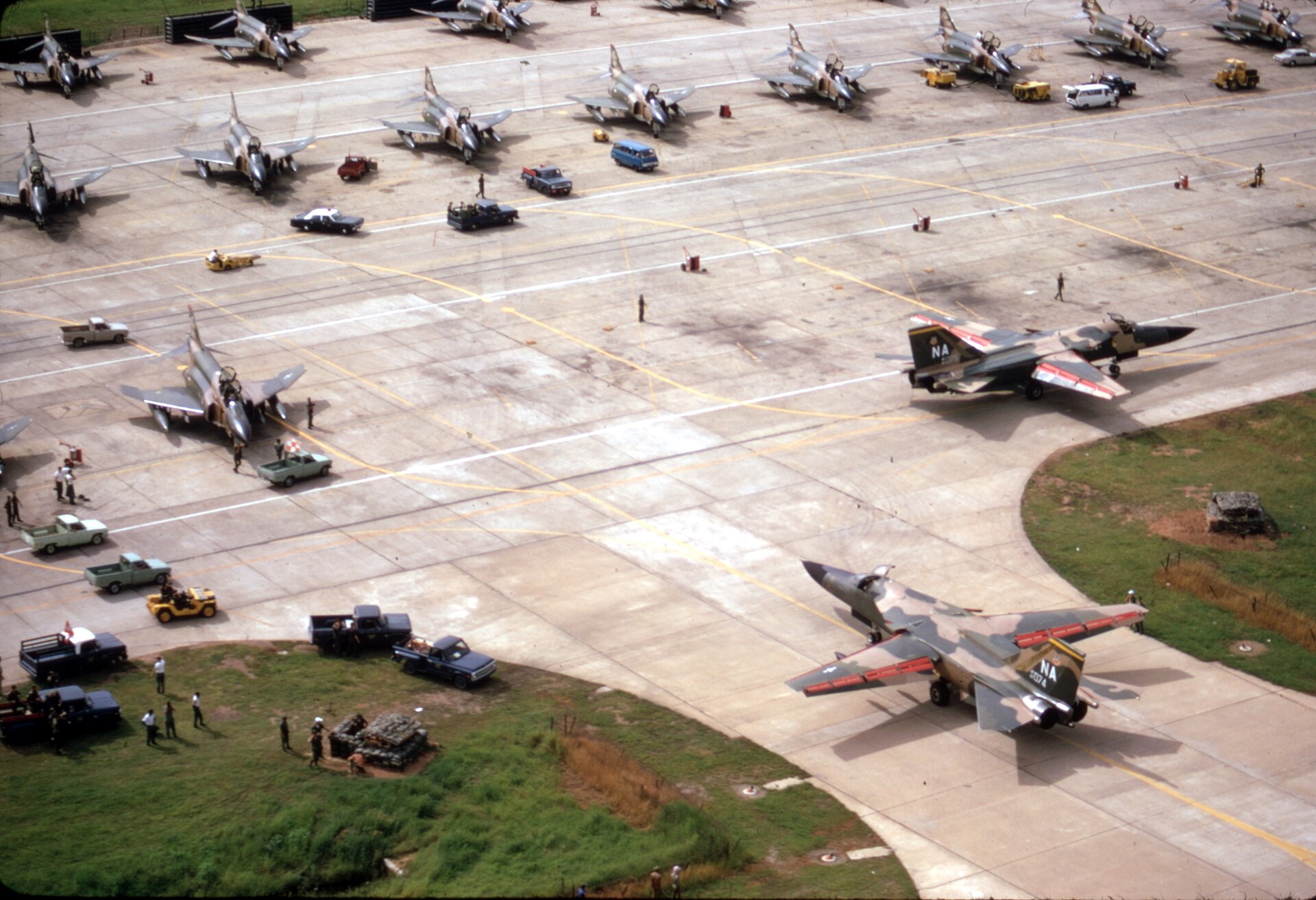Two F-111As of the 474th Tactical Fighter Wing taxiing on the flight line at Takhli, with F-4 Phantoms in the background