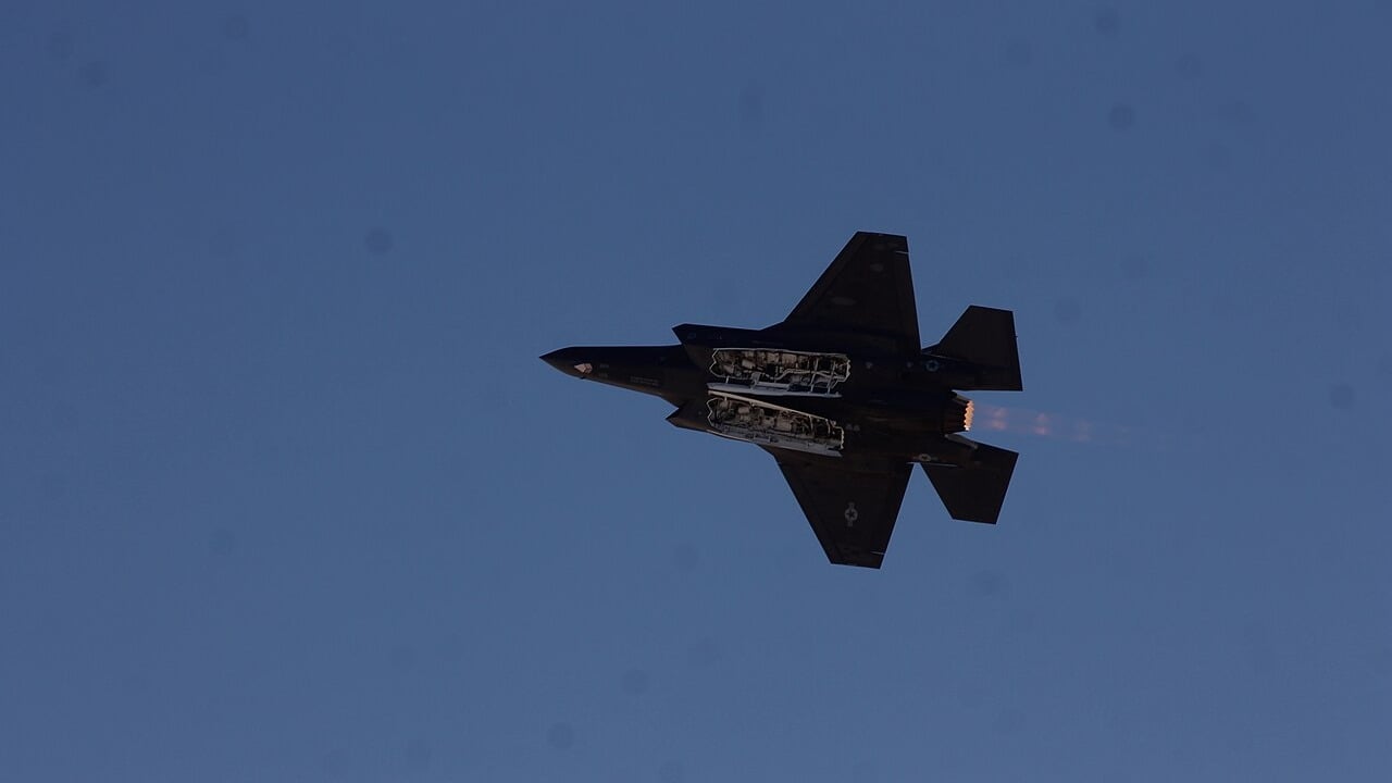 An F-35A Lightning II banking in flight with both weapons bay doors hanging open