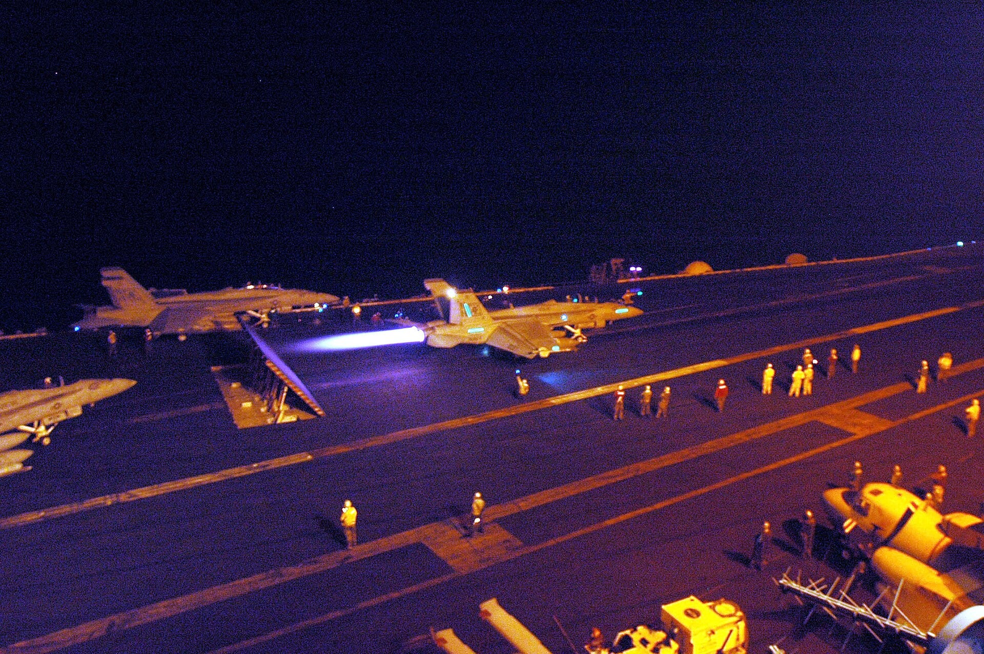 An F/A-18F Super Hornet of VFA-41 in full afterburner with a blue exhaust plume before a night catapult launch in 2005