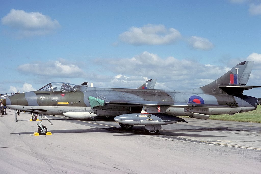 A camouflaged Hawker Hunter FGA.9 ground attack fighter parked with underwing drop tanks