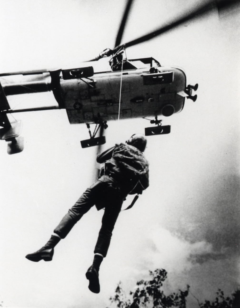 A USAF pararescueman hanging below an HH-43 Huskie in Southeast Asia
