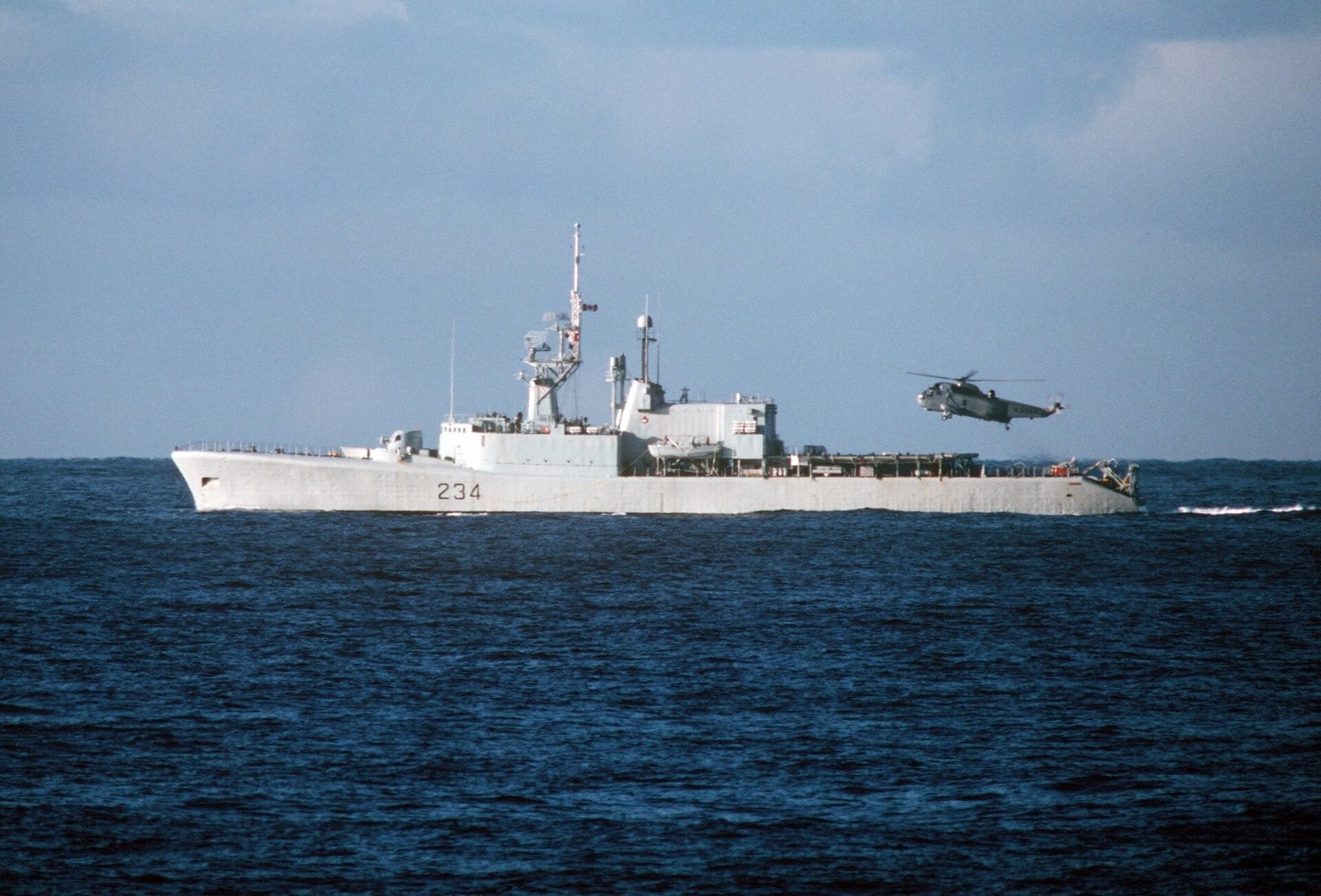 HMCS Assiniboine, pennant 234, underway with her CH-124 Sea King airborne off the port quarter