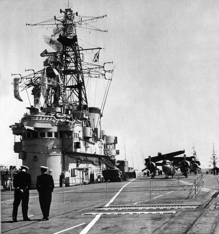 Two officers on the flight deck of HMCS Bonaventure in April 1959, with Trackers parked aft