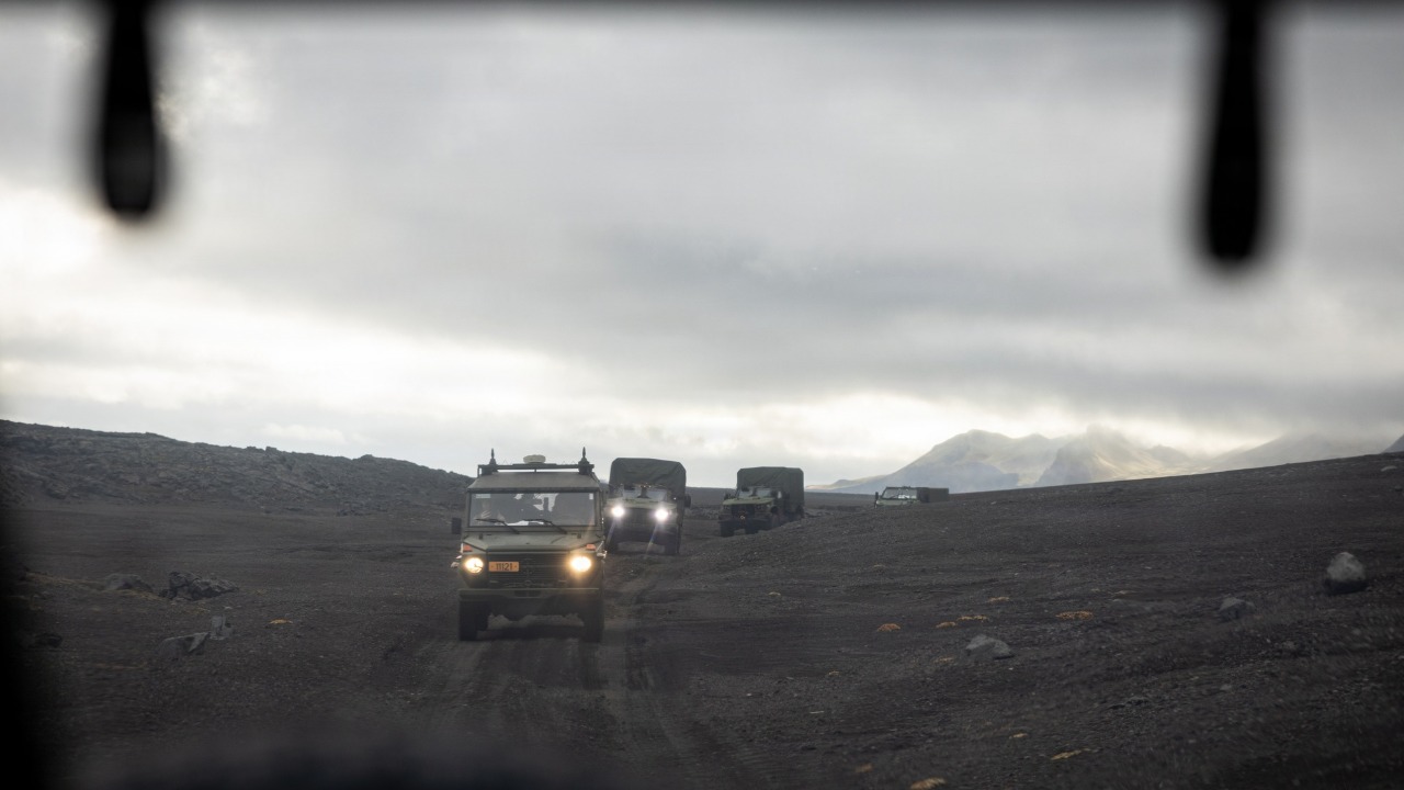 A military convoy driving across black volcanic terrain on Jan Mayen island
