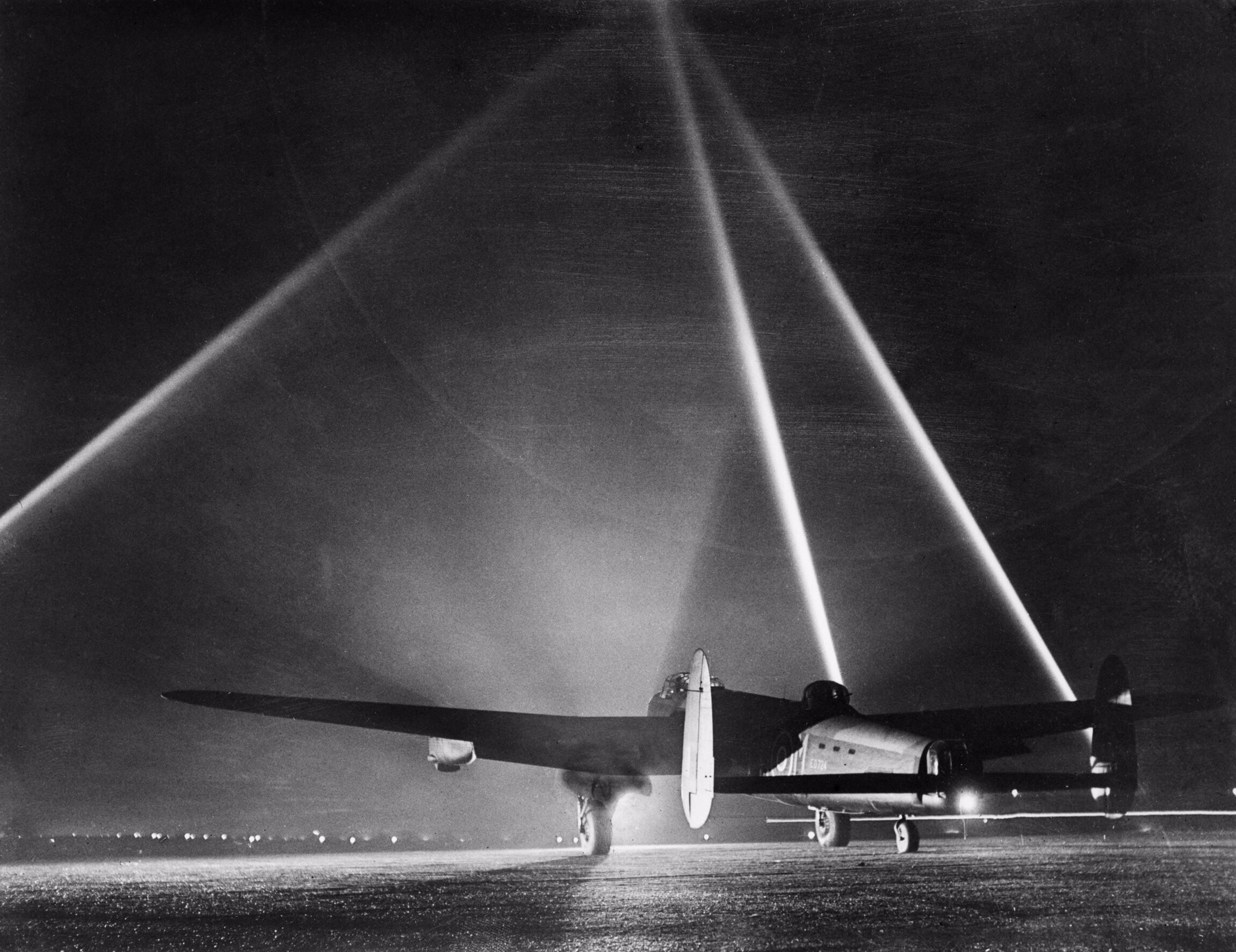 Lancaster on the flarepath at night An Avro Lancaster pauses on the flarepath before a night raid, searchlights forming a cone behind