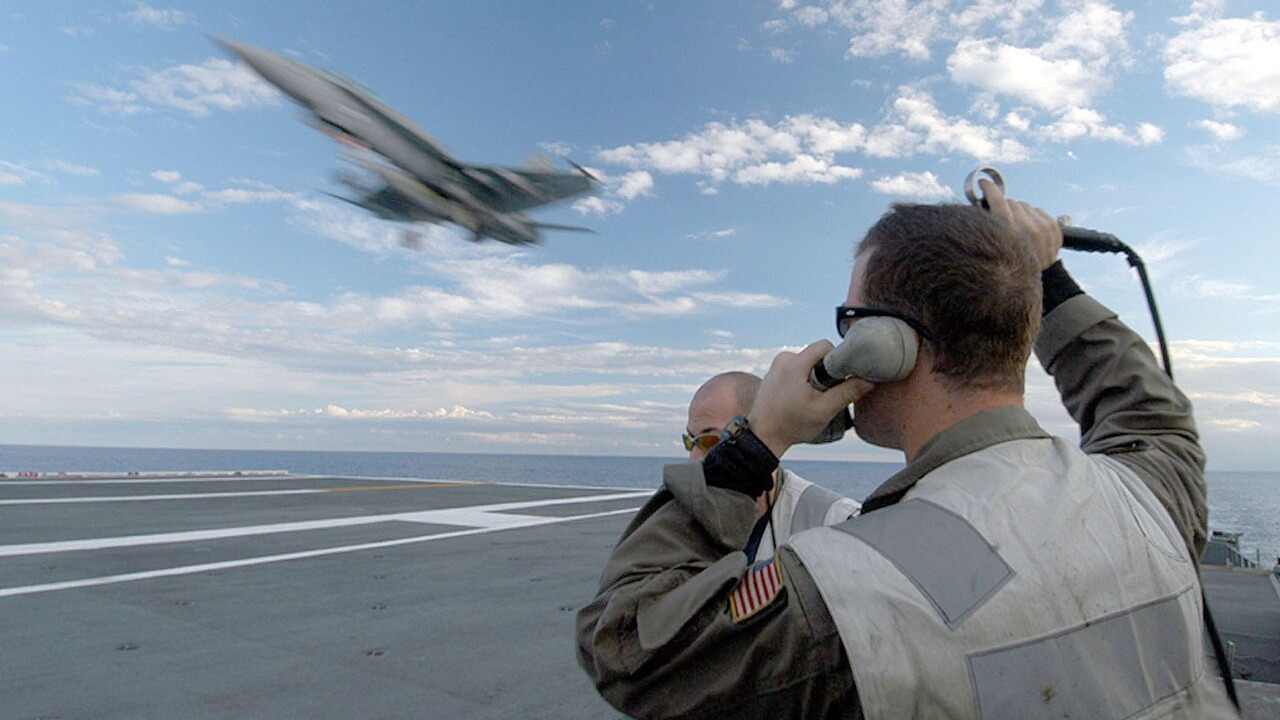 Landing signal officers on the LSO platform as an F/A-18 approaches USS John F. Kennedy