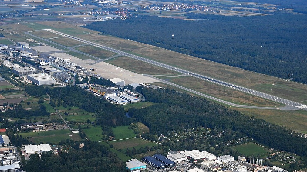 Aerial view of Nuremberg Airport showing its single runway, apron and terminal surrounded by forest and suburbs