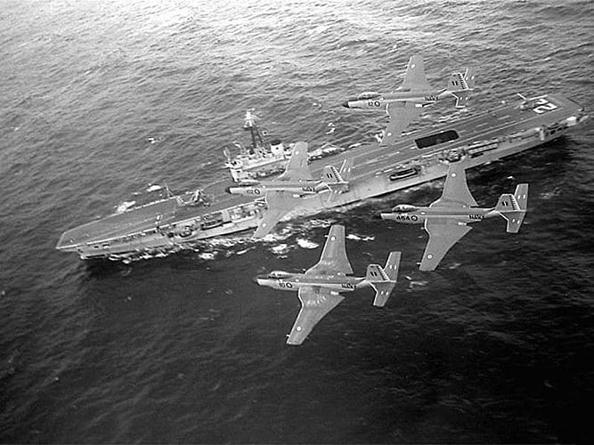 Four Royal Canadian Navy F2H-3 Banshees in formation above HMCS Bonaventure at sea