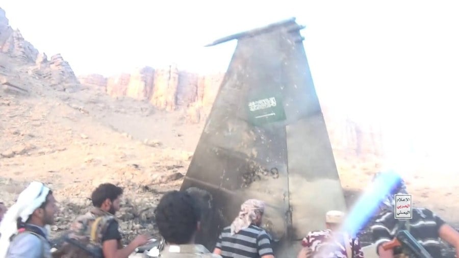 A tailfin from the destroyed F-15 carrying the Saudi flag marking, with armed men in the foreground
