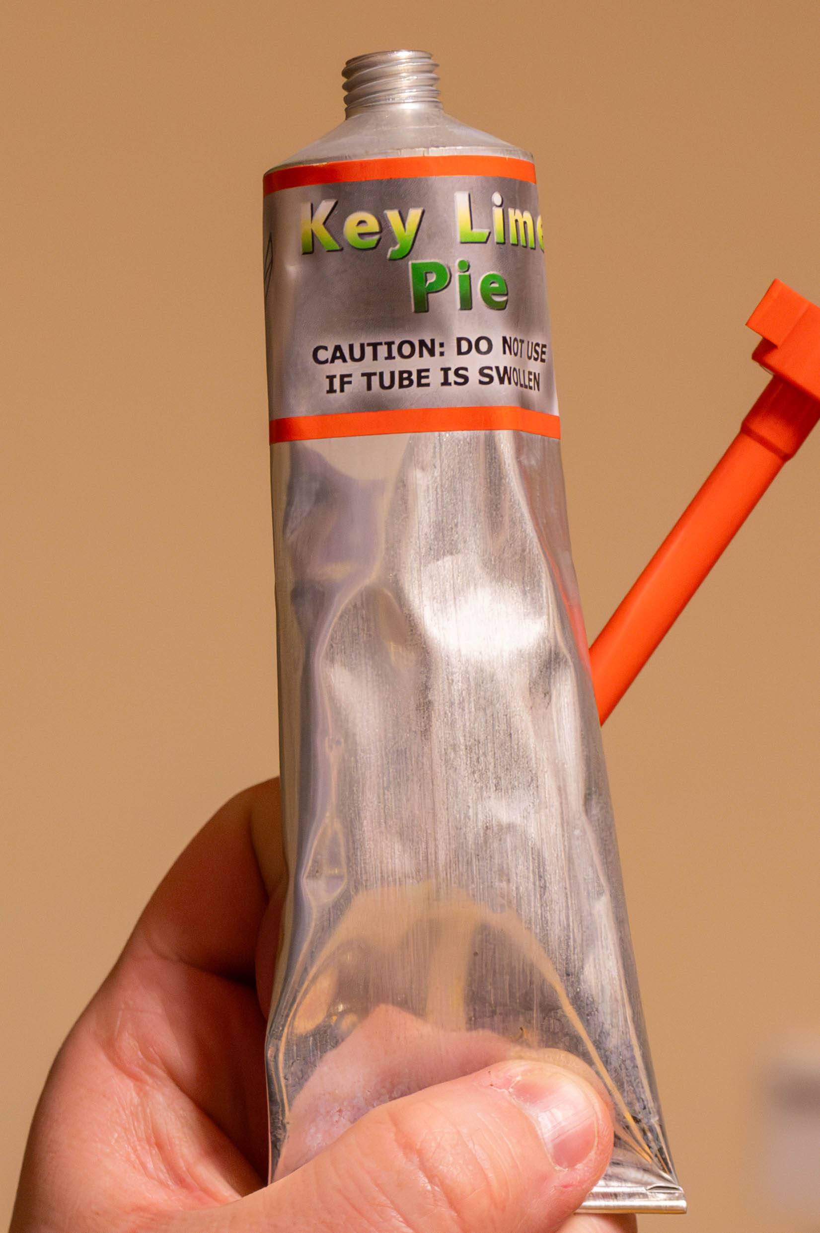 A hand holding a metal tube of U-2 key lime pie tube food with the orange feeding straw attached