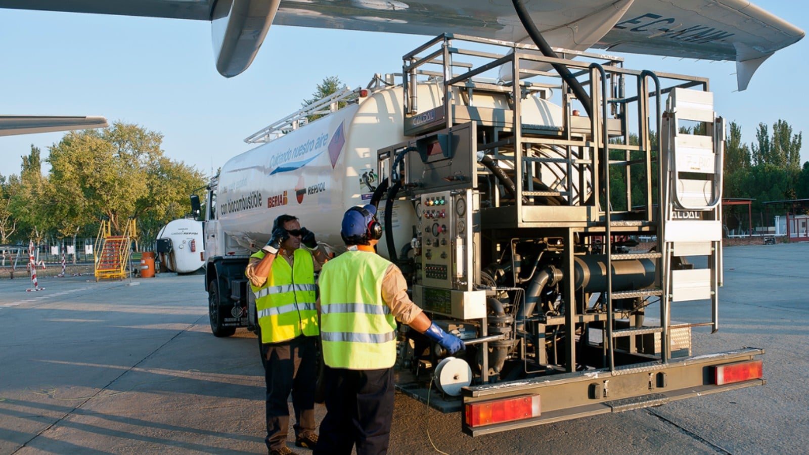 Ground crew beside a fuel bowser coupled to an airliner wing
