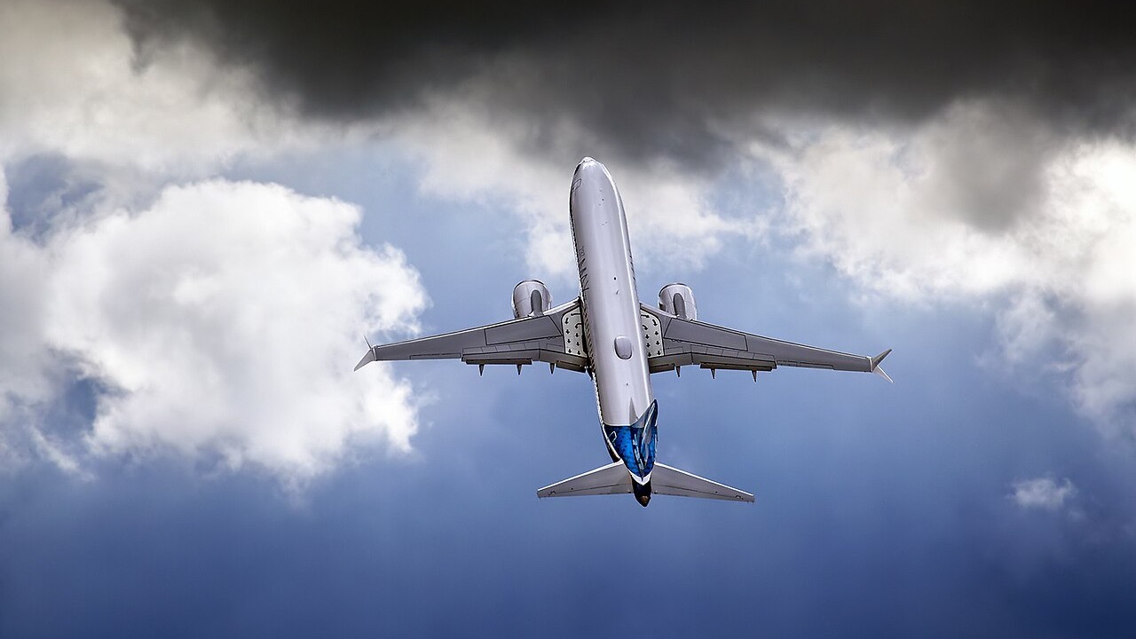 A Boeing 737-8 MAX in Boeing house colours climbing steeply under dark clouds