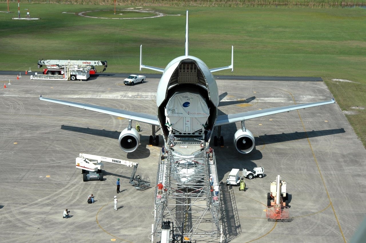An Airbus Beluga with its nose door raised at the Kennedy Space Center Shuttle Landing Facility as the ESA Columbus module is unloaded onto a platform