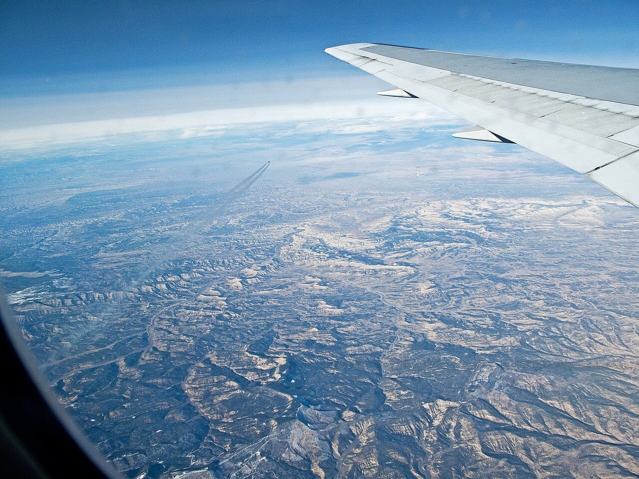 Another airliner and its contrail crossing below a Boeing 767 over the deserts of Arizona or Utah