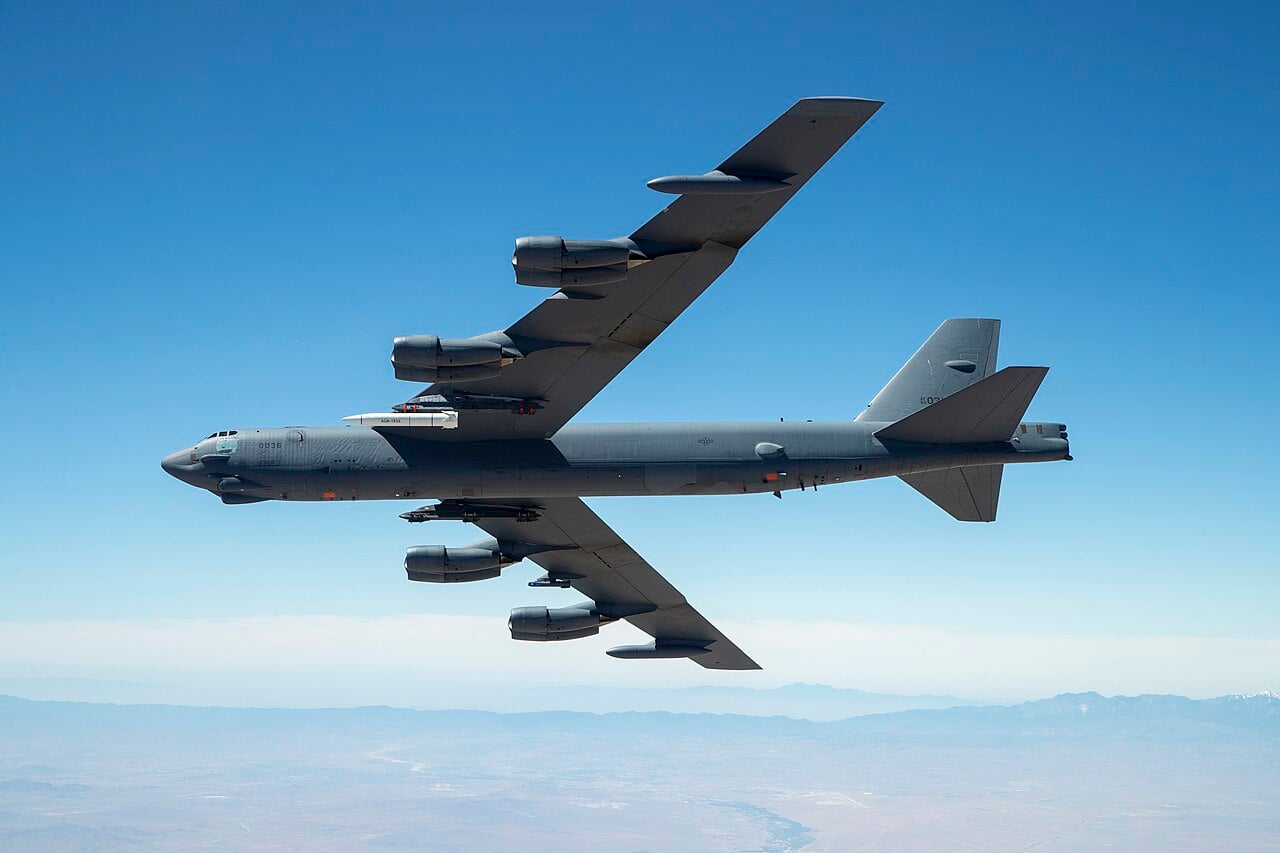 A B-52 Stratofortress in flight over the California desert carrying an ARRW test article under its left wing