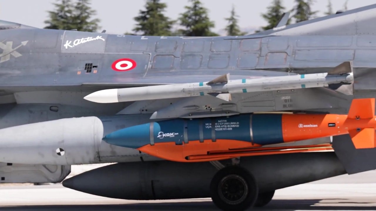 An orange and blue ASELSAN KGK-84 winged guidance kit fitted to a 2,000 lb bomb under the wing of a Turkish Air Force F-16
