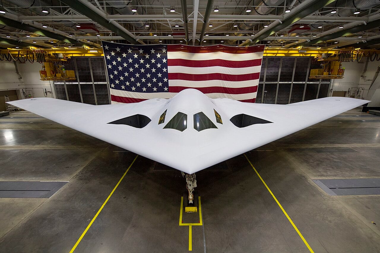 B-21 Raider seen head-on inside a hangar in front of a US flag