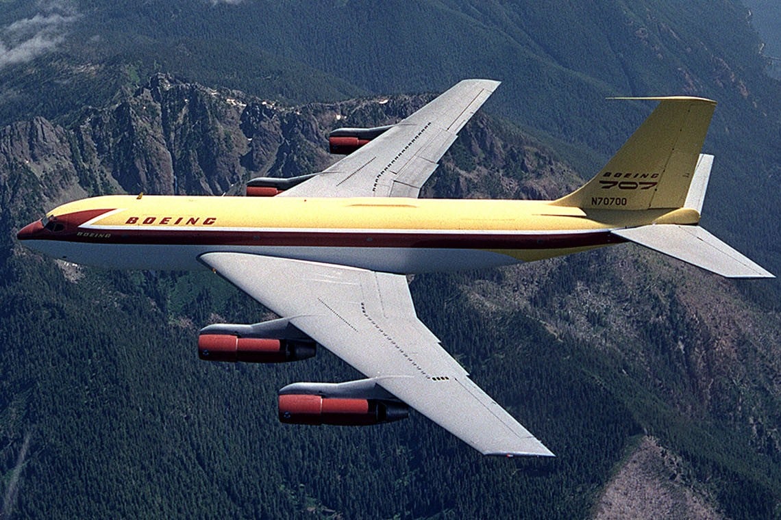 The yellow and brown Boeing 367-80 Dash 80 jet transport prototype N70700 flying over mountains in Washington State