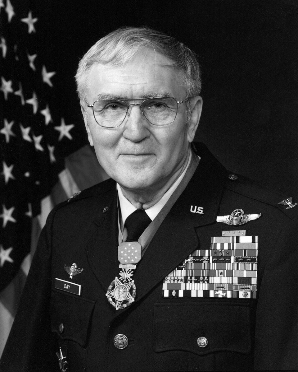 Official portrait of US Air Force Col. George E. Bud Day in service dress wearing the Medal of Honor, with an American flag behind him
