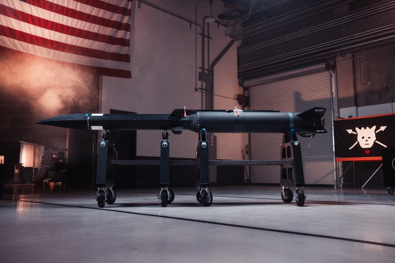 A black Castelion Blackbeard hypersonic missile on a transport cart in a hangar in front of a US flag