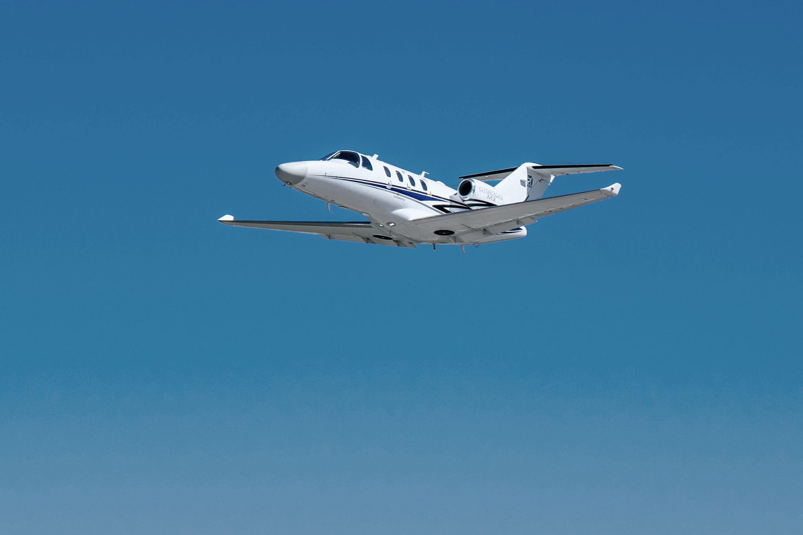 Cessna Citation M2 Gen3 light jet climbing against a clear blue sky