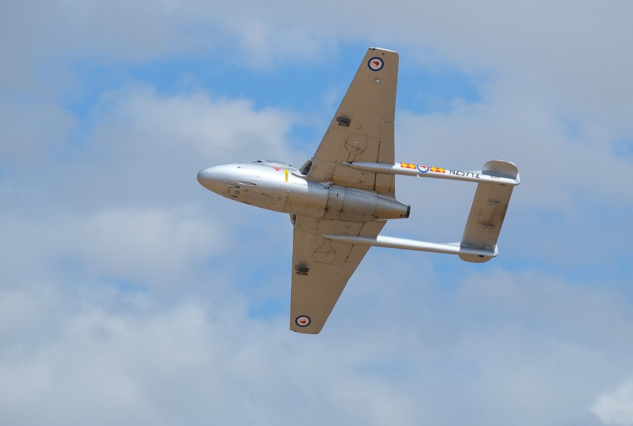 A silver de Havilland Vampire T.11 flying overhead showing its twin-boom planform