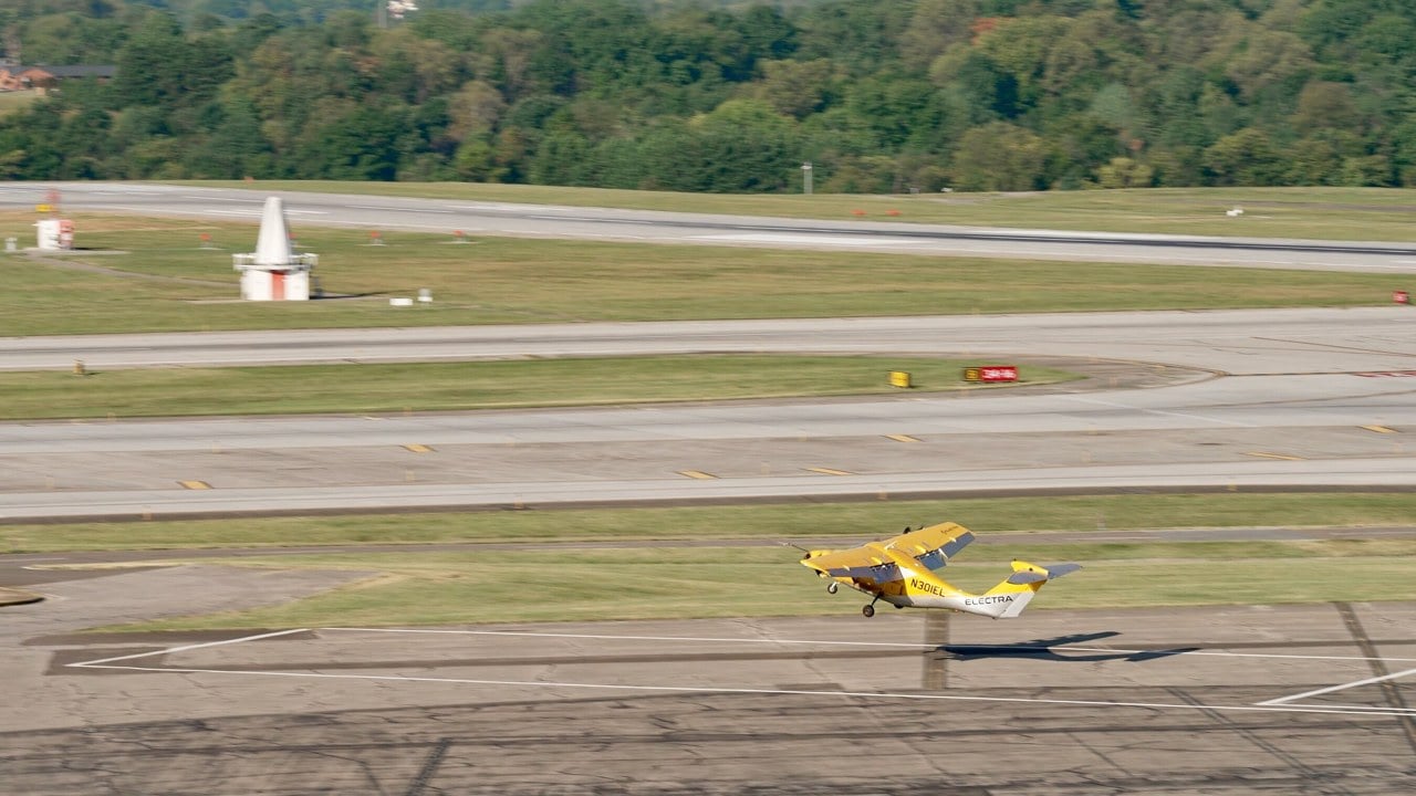 The yellow Electra EL2 hybrid-electric demonstrator lifting off from a small marked landing area at Roanoke-Blacksburg Regional Airport