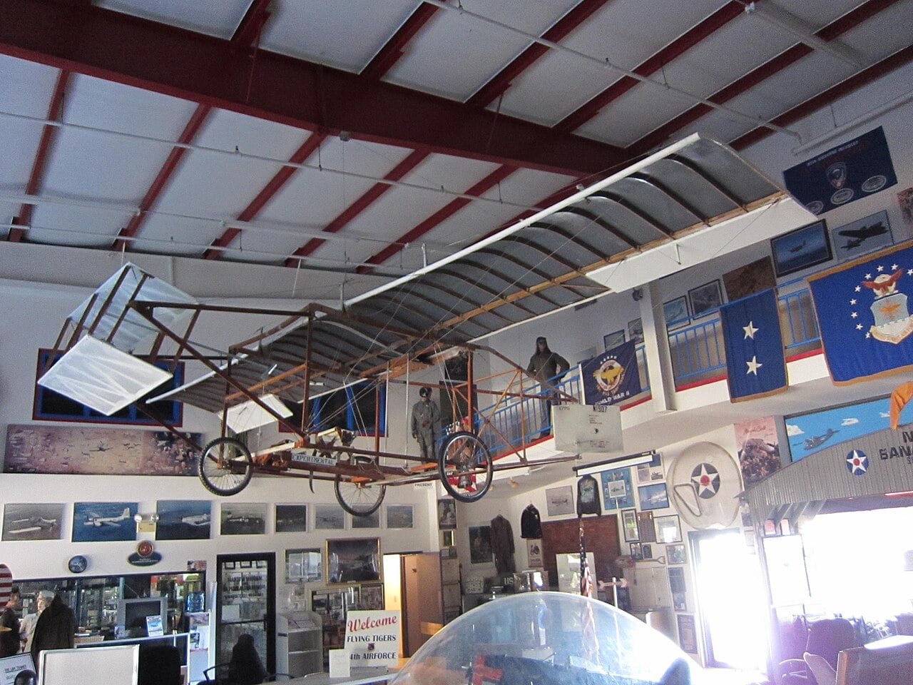 Replica of Ben Epps's first monoplane with bicycle wheels and an open wooden frame hanging in a museum hangar