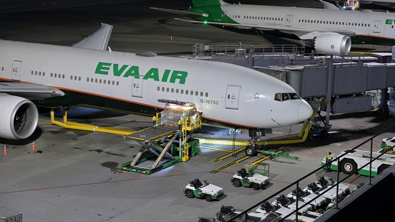 A pallet of cargo on a loader being lifted into the forward hold of an EVA Air Boeing 777-300ER at night