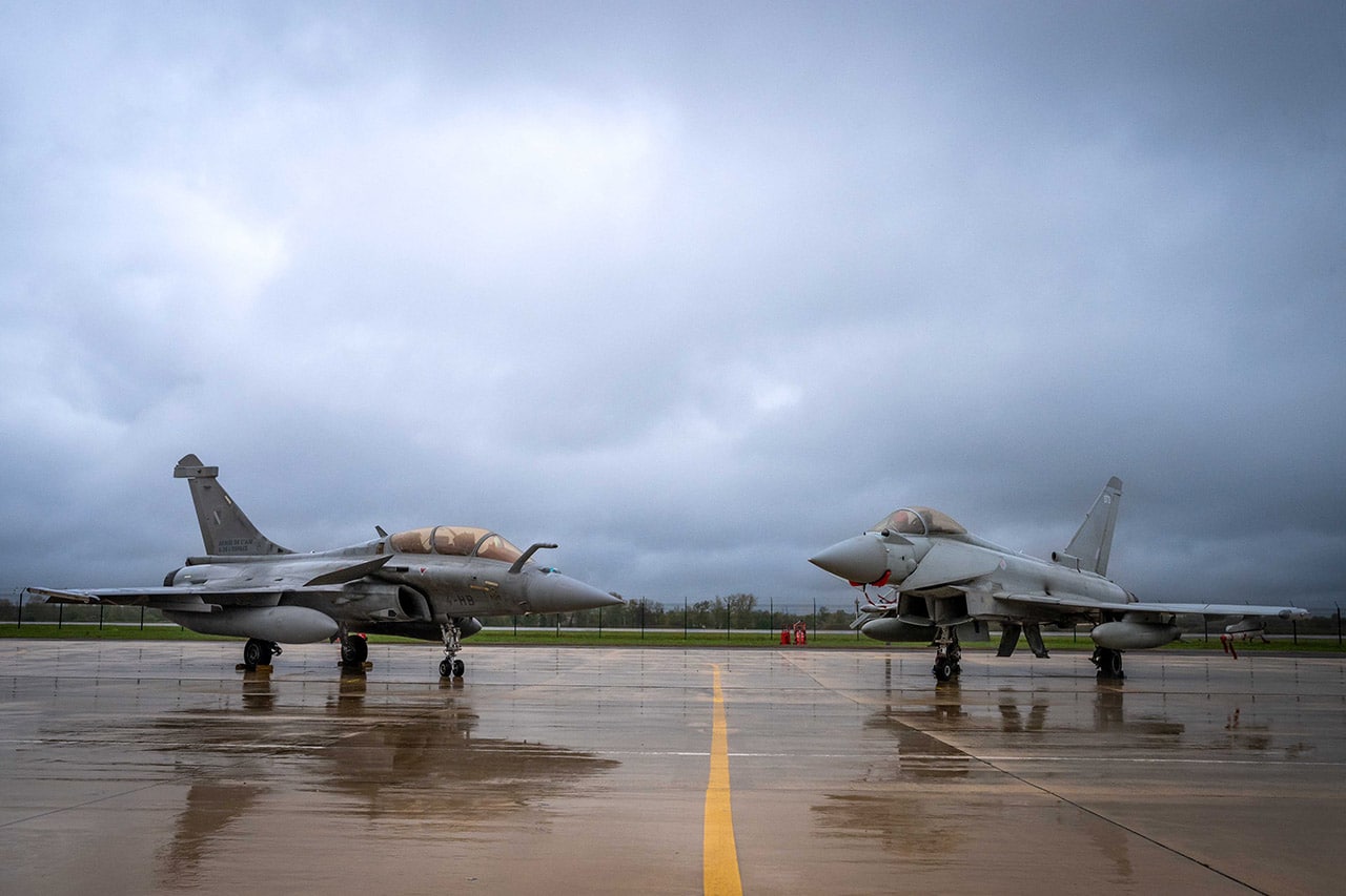 A French Rafale B and an RAF Typhoon FGR4 parked side by side on a wet ramp at Saint-Dizier