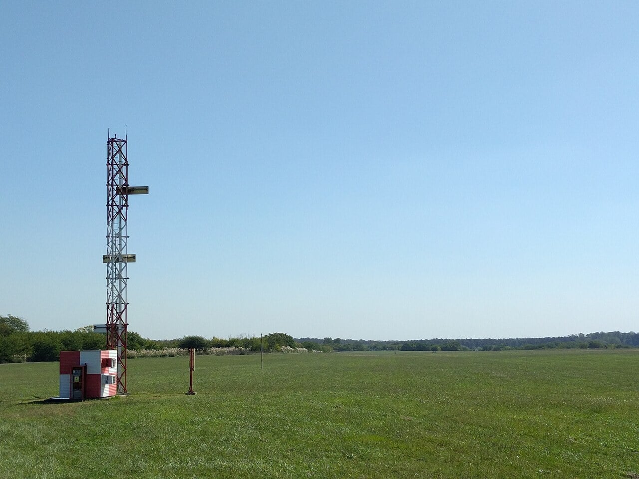 A red and white lattice mast carrying ILS glideslope antennas beside runway 11 at Ezeiza airport, Buenos Aires