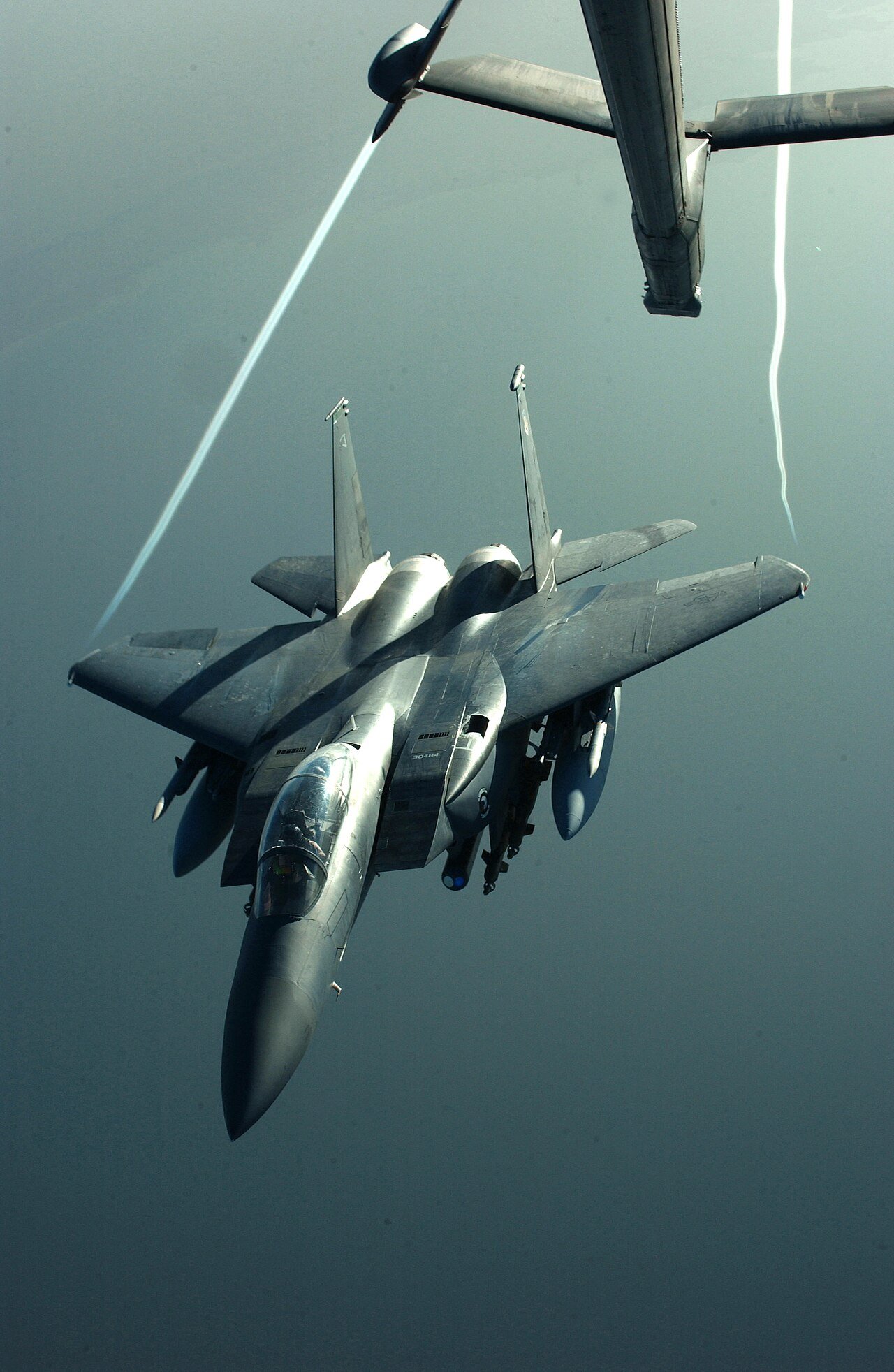 F-15E Strike Eagle below a KC-10 tanker with white condensation trails streaming from its wingtips