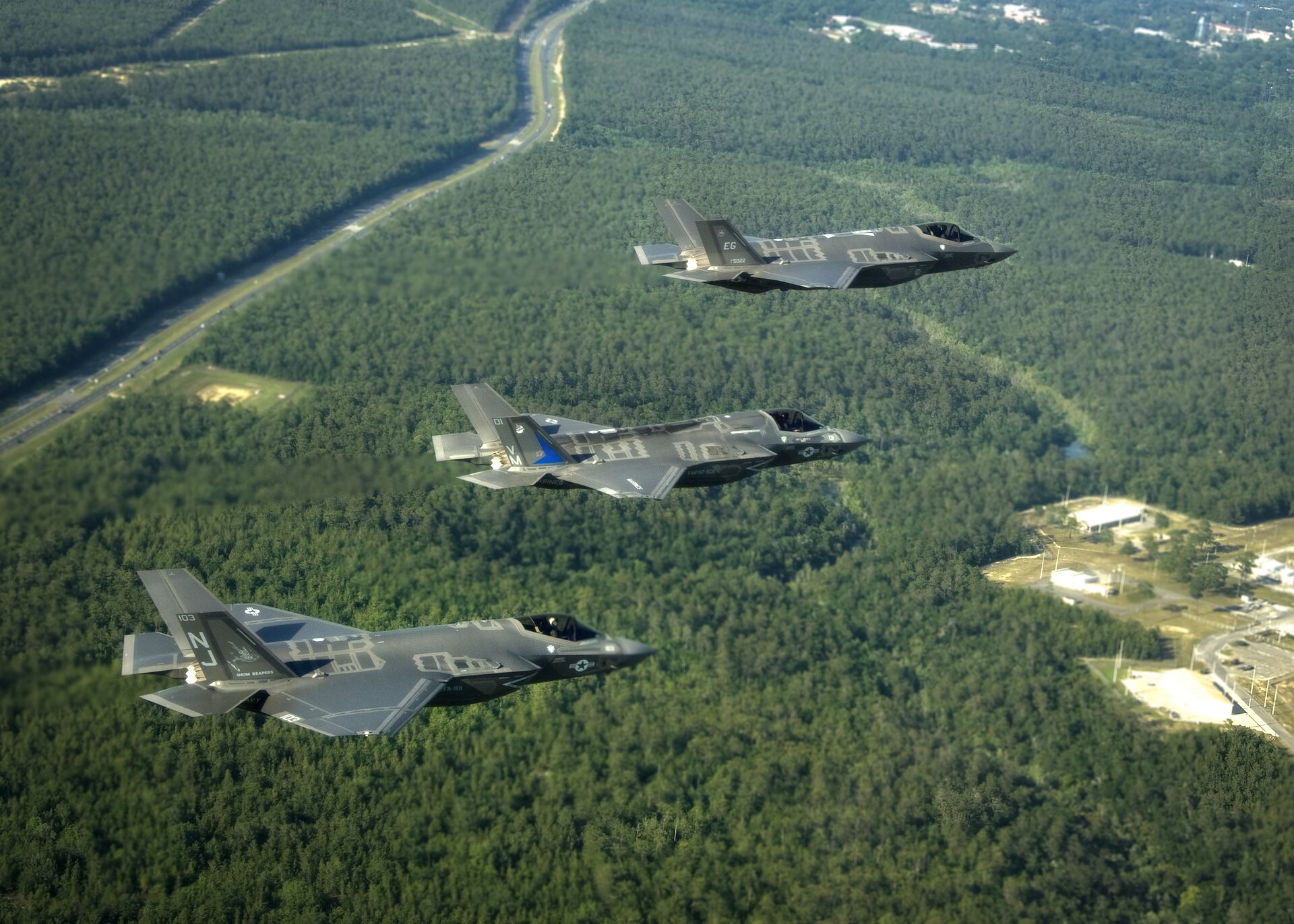 Three F-35 Lightning II variants flying in formation above woodland