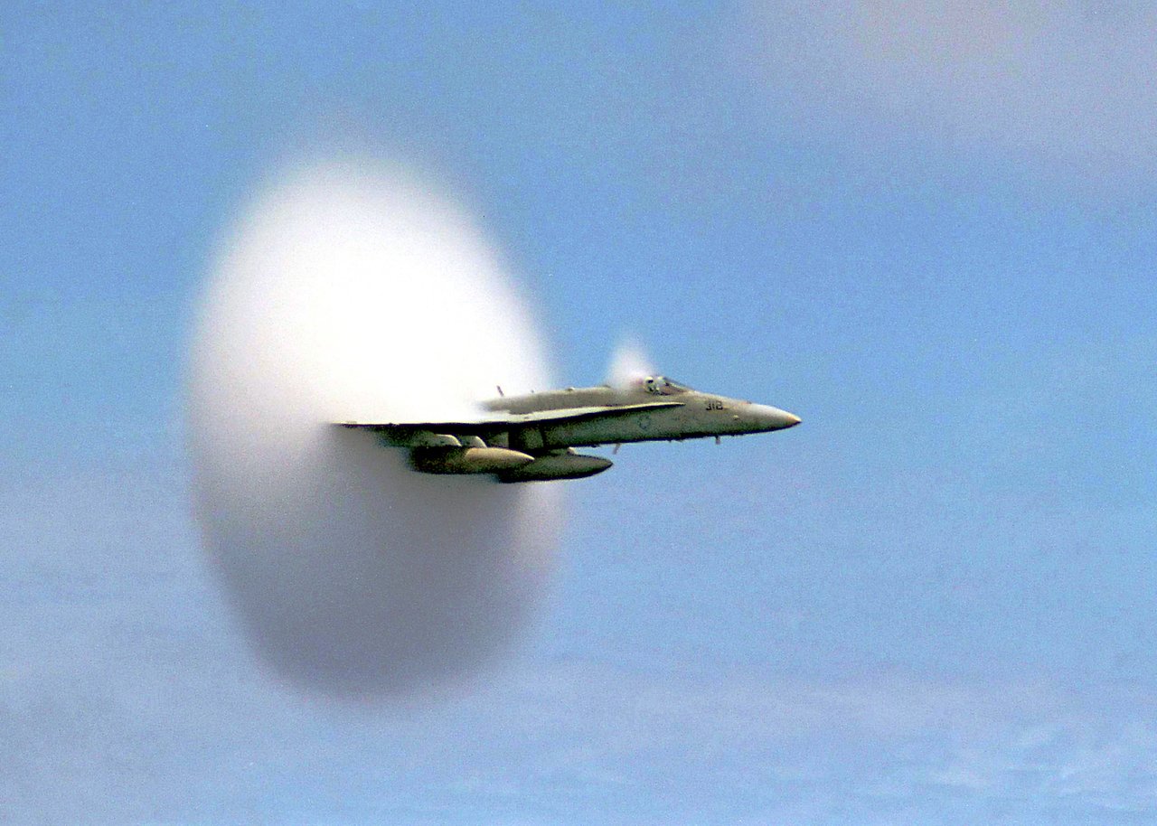 US Navy F/A-18C Hornet emerging from a bell-shaped vapor cone over the sea, photographed by Ensign John Gay in 1999