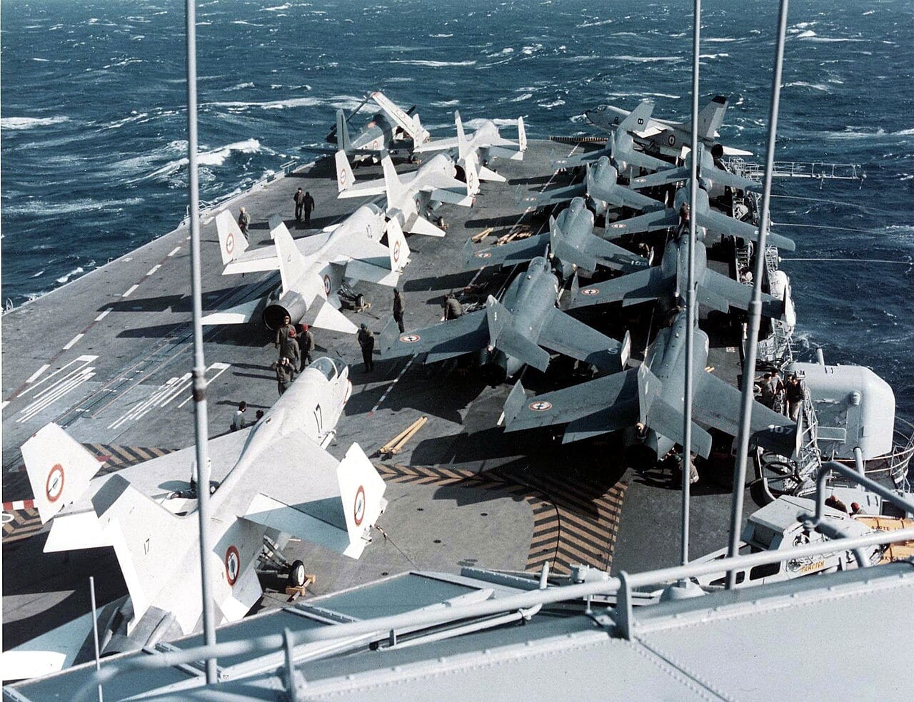 The forward flight deck of a French aircraft carrier in the 1970s crowded with Étendard IV jets, F-8 Crusaders and an Alizé