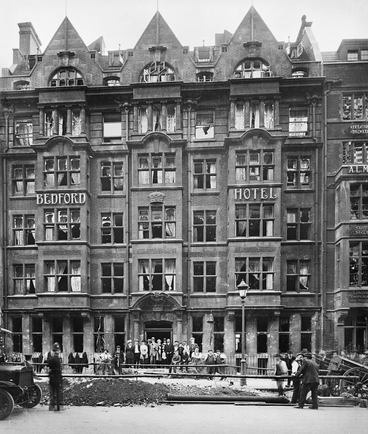 Crowd outside the Bedford Hotel on Southampton Row in London with broken windows and a bomb crater in the road, September 1917