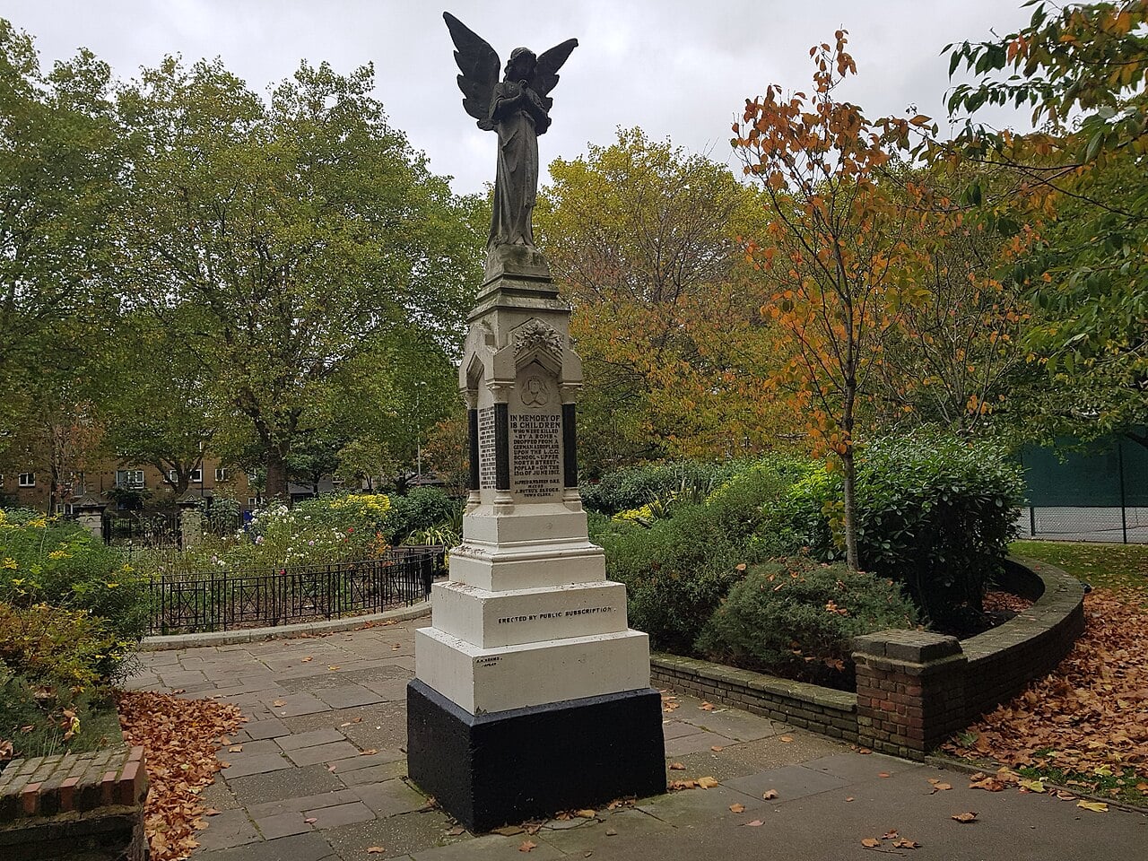 Angel statue on the white memorial to the 18 children of Upper North Street School in Poplar Recreation Ground, London