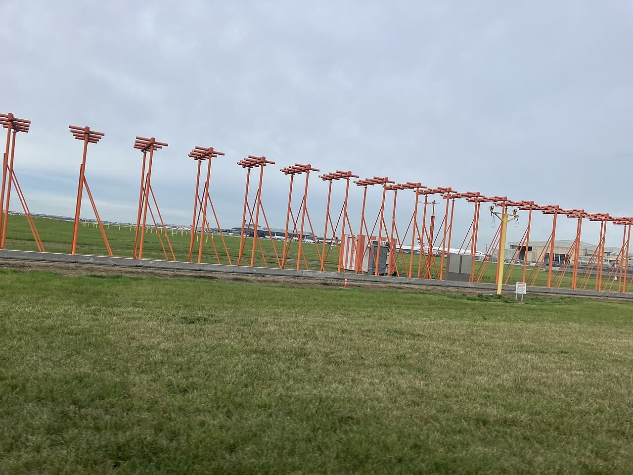 A long row of orange ILS localizer antennas on masts at the end of a runway at London Heathrow Airport